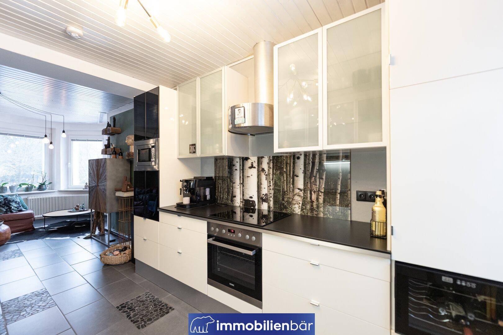 Moderne Küche mit integrierten Geräten, Glasfronten und offenem Übergang zum Wohnbereich.