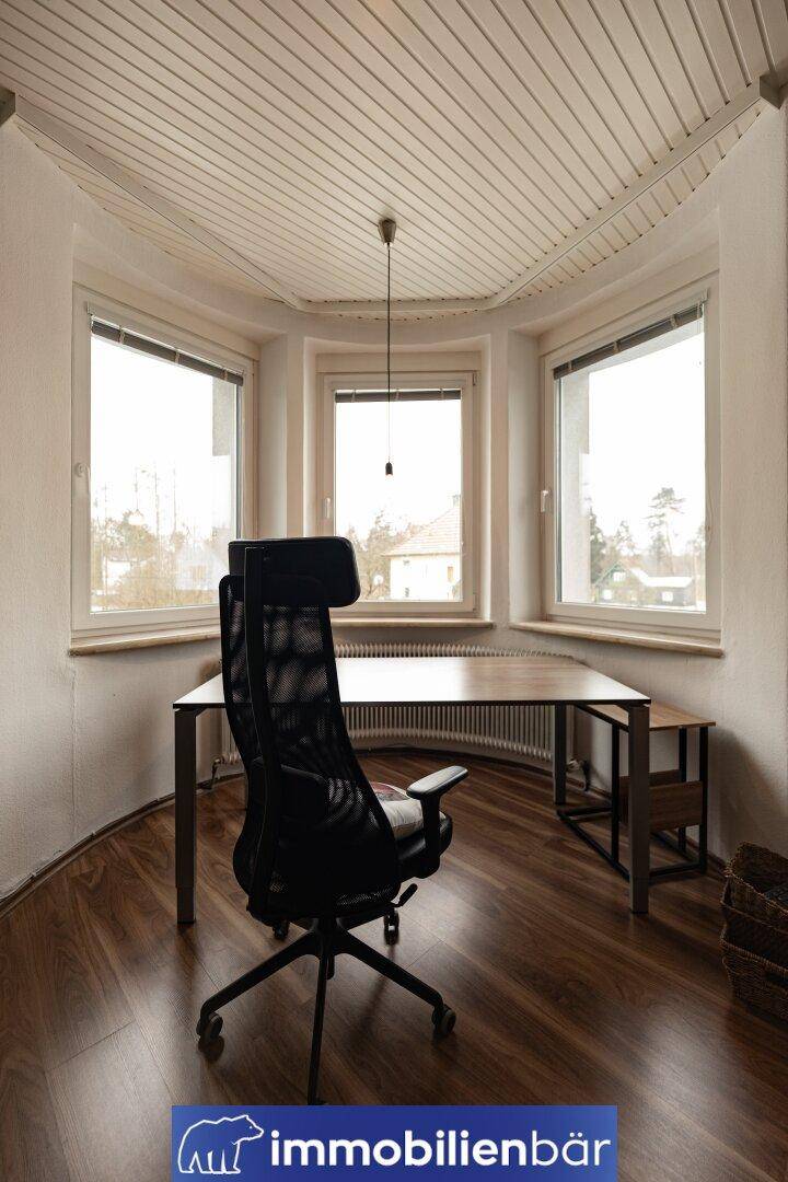 Helles Arbeitszimmer mit Schreibtisch, ergonomischem Stuhl und großen Fenstern mit Ausblick.