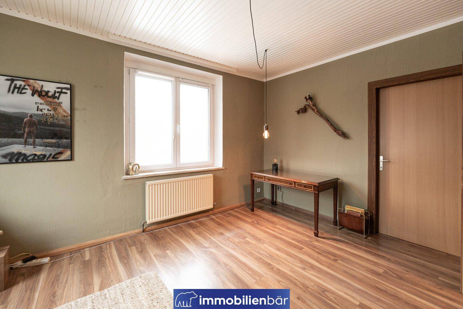 Heller Raum mit einem Schreibtisch, Heizkörper und einem großen Fenster.