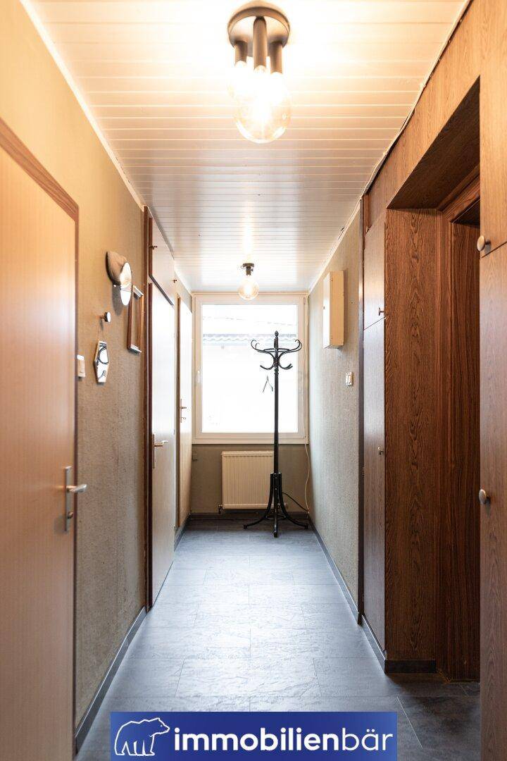 Langer Flur mit Fenster, Garderobe und hellem Deckenpaneel.