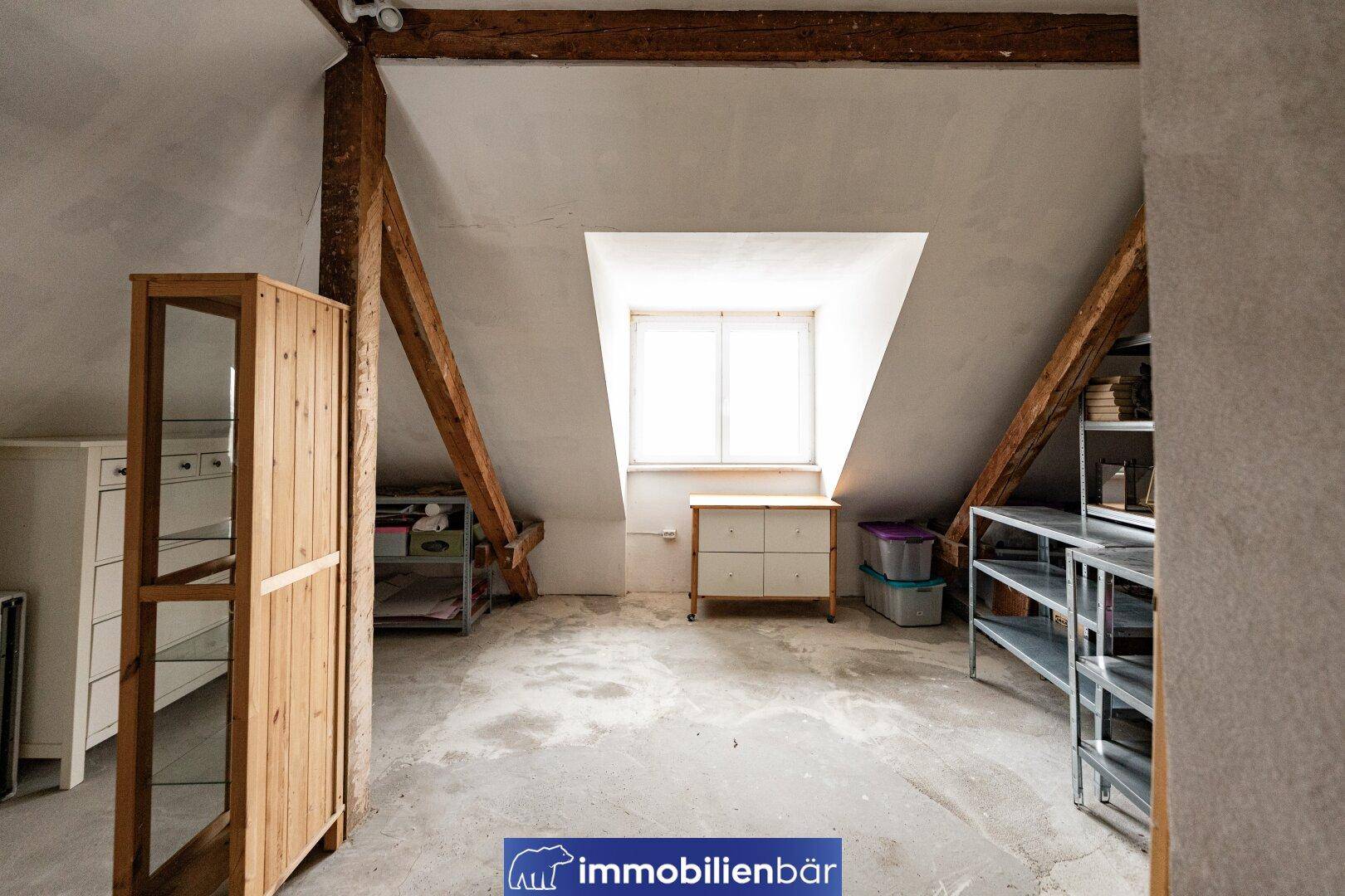 Dachboden mit sichtbaren Holzbalken, Dachfenster und Stauraum.