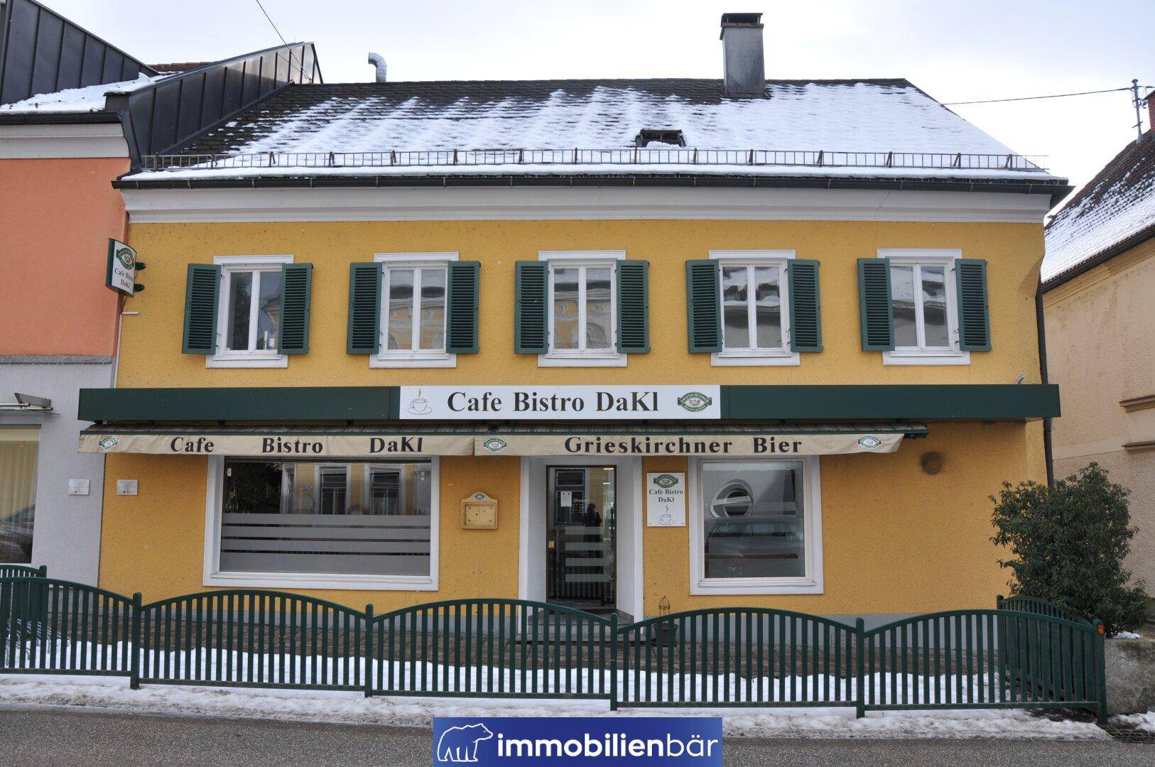 Gelbes Gebäude mit grünen Fensterläden und einer Markise, das ein Café und Bistro beherbergt.