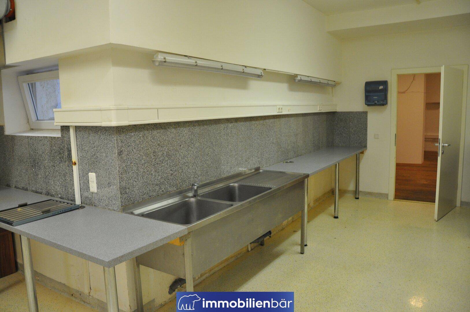 Geräumige Gewerbeküche mit Edelstahlspülbecken, langen Arbeitsflächen und einem Fenster für Belüftung.