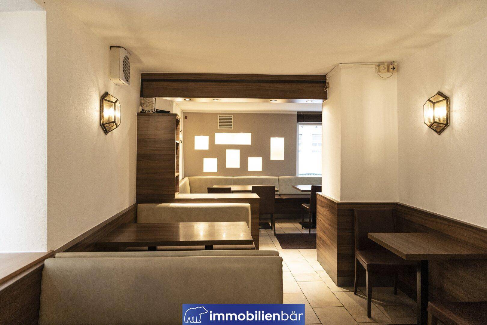 Gemütlicher Gastraum mit Sitzbänken, Holztischen und Wandleuchten, ideal für ein Café oder Bistro.