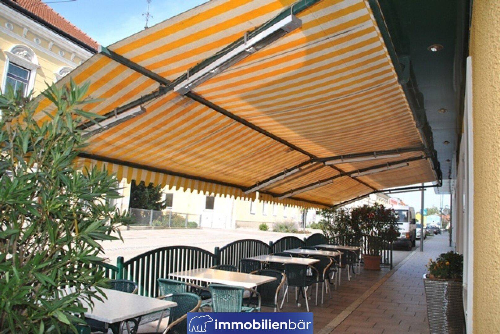 Außenbereich eines Cafés mit gestreiften Markisen, Tischen und Stühlen, ideal für sonnige Tage.