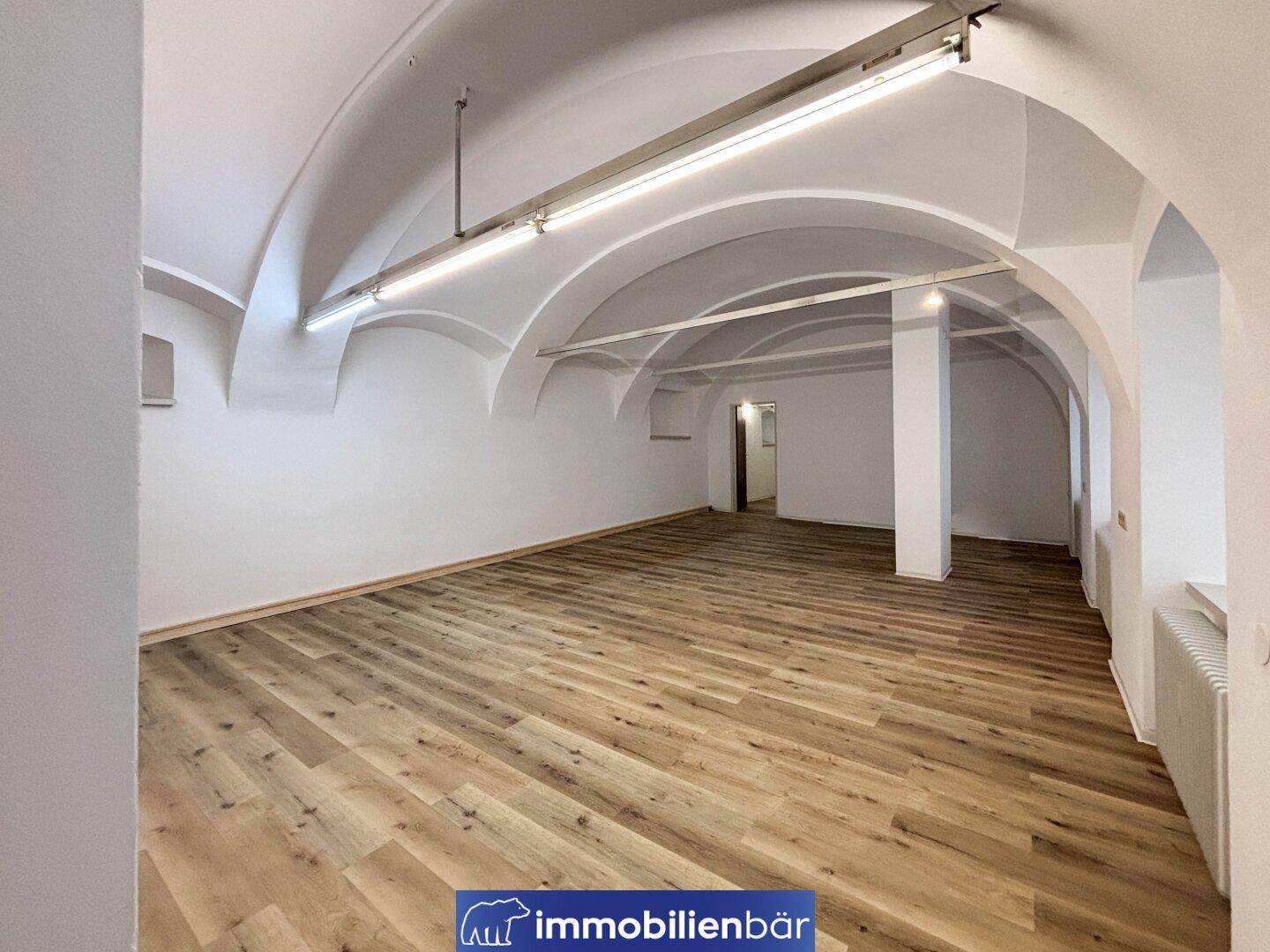 Weitläufiger Raum mit charakteristischen Gewölbedecken und modernem Laminatboden, der vielseitige Gestaltungsmöglichkeiten bietet.