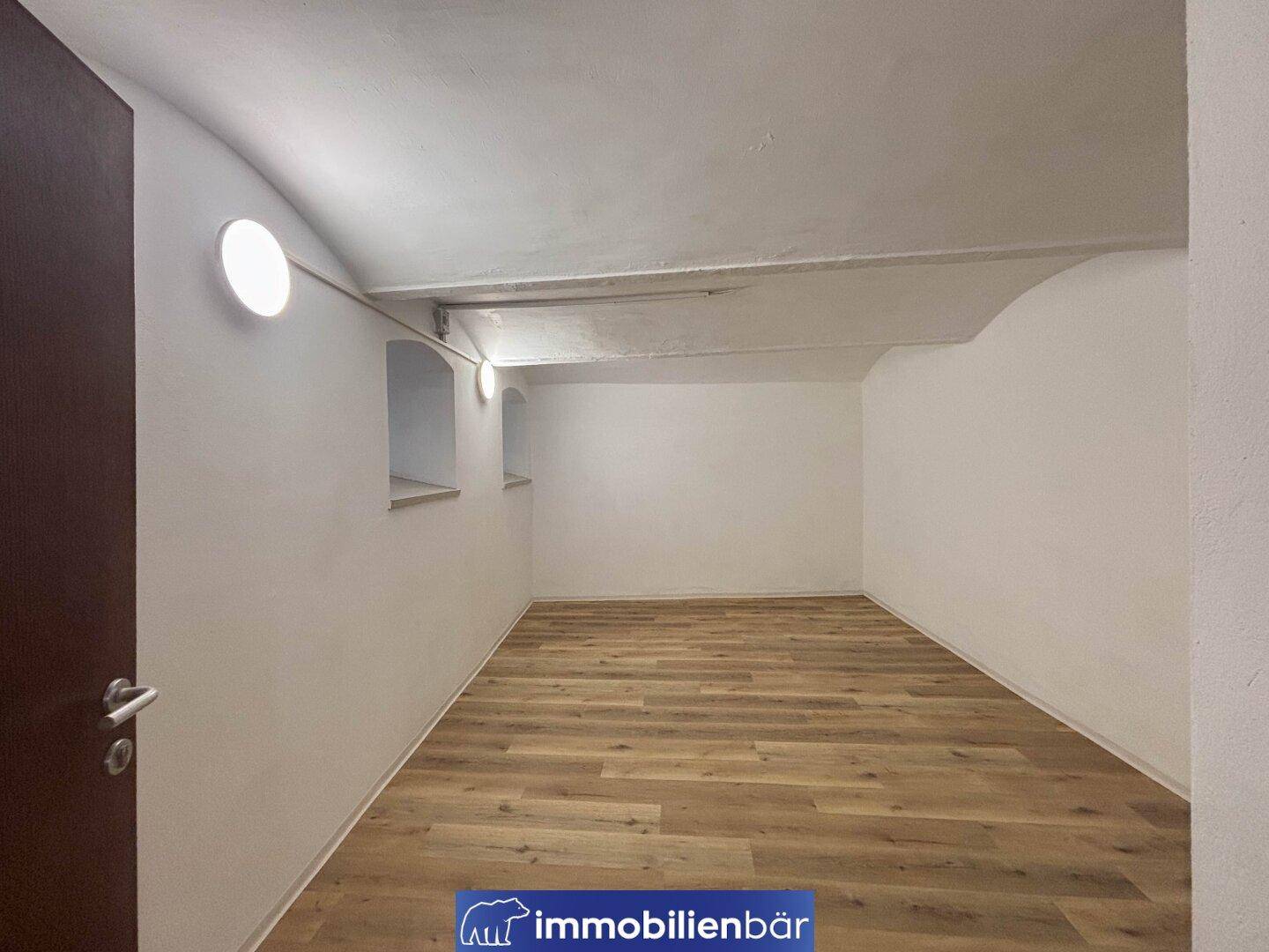 Kleinerer Raum mit niedriger Decke und Holzboden, möglicherweise ein Keller oder Abstellraum, mit kleinen Nischenfenstern.
