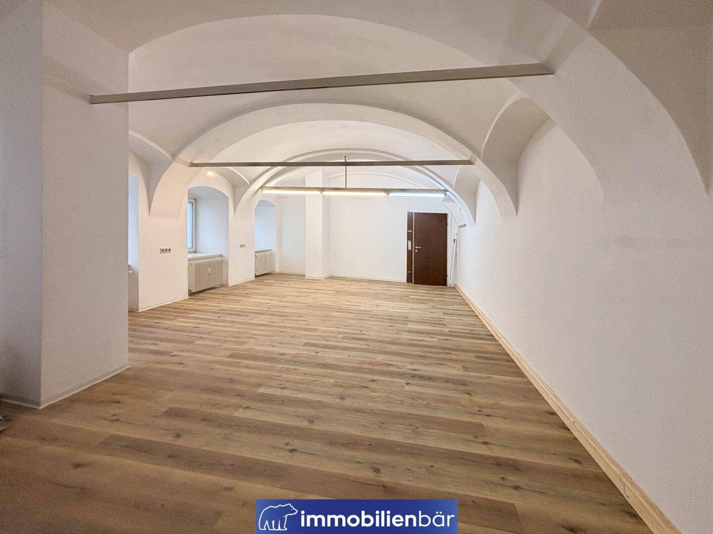Großer, offener Raum mit beeindruckenden Gewölbedecken und neuem Laminatboden, der eine helle und einladende Atmosphäre schafft.