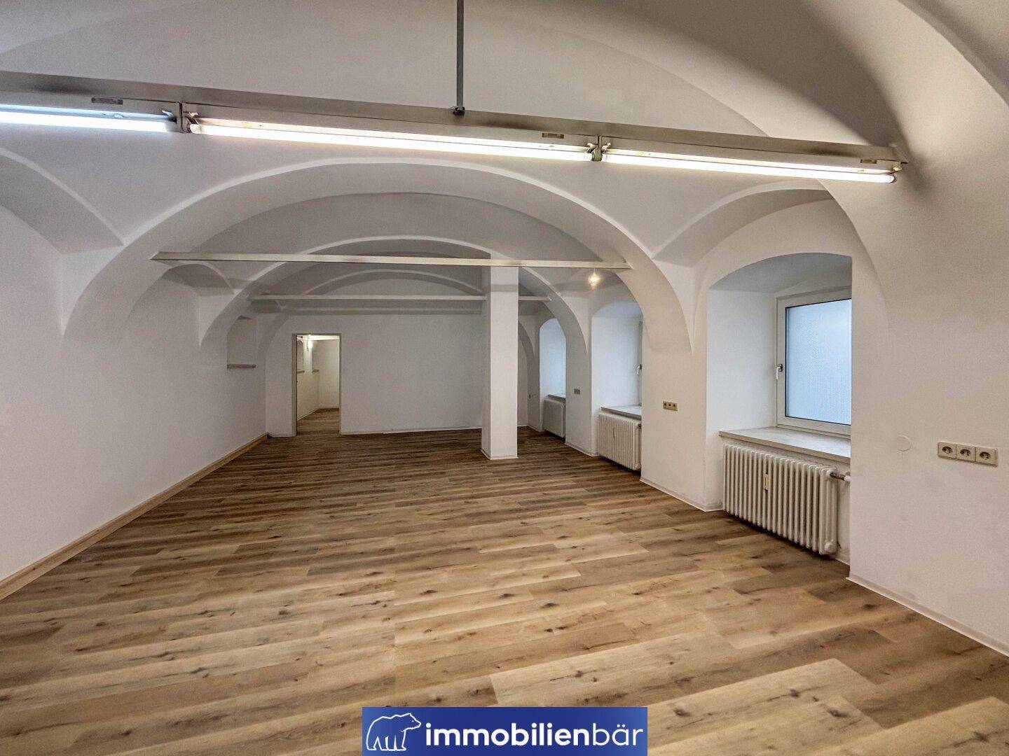 Heller Wohnraum mit eleganten Gewölbedecken, neuen Böden und traditionellen Heizkörpern unter den Fenstern, bereit zum Einzug.