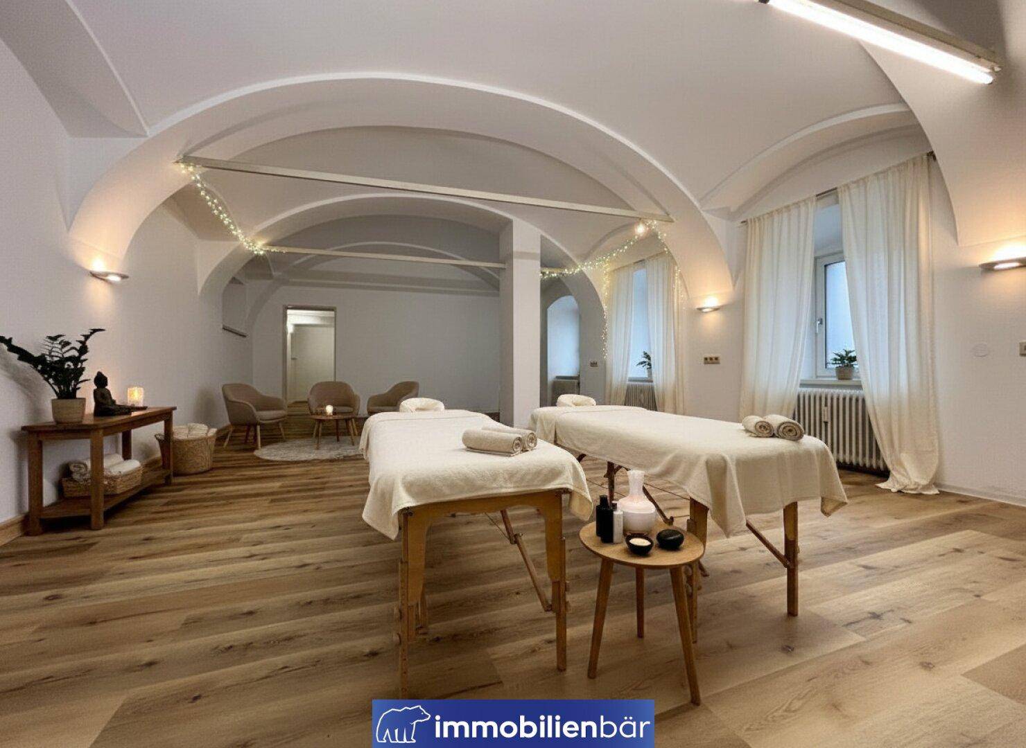 Heller Behandlungsraum mit zwei Massageliegen, Holzboden und stimmungsvoller Beleuchtung unter gewölbter Decke.