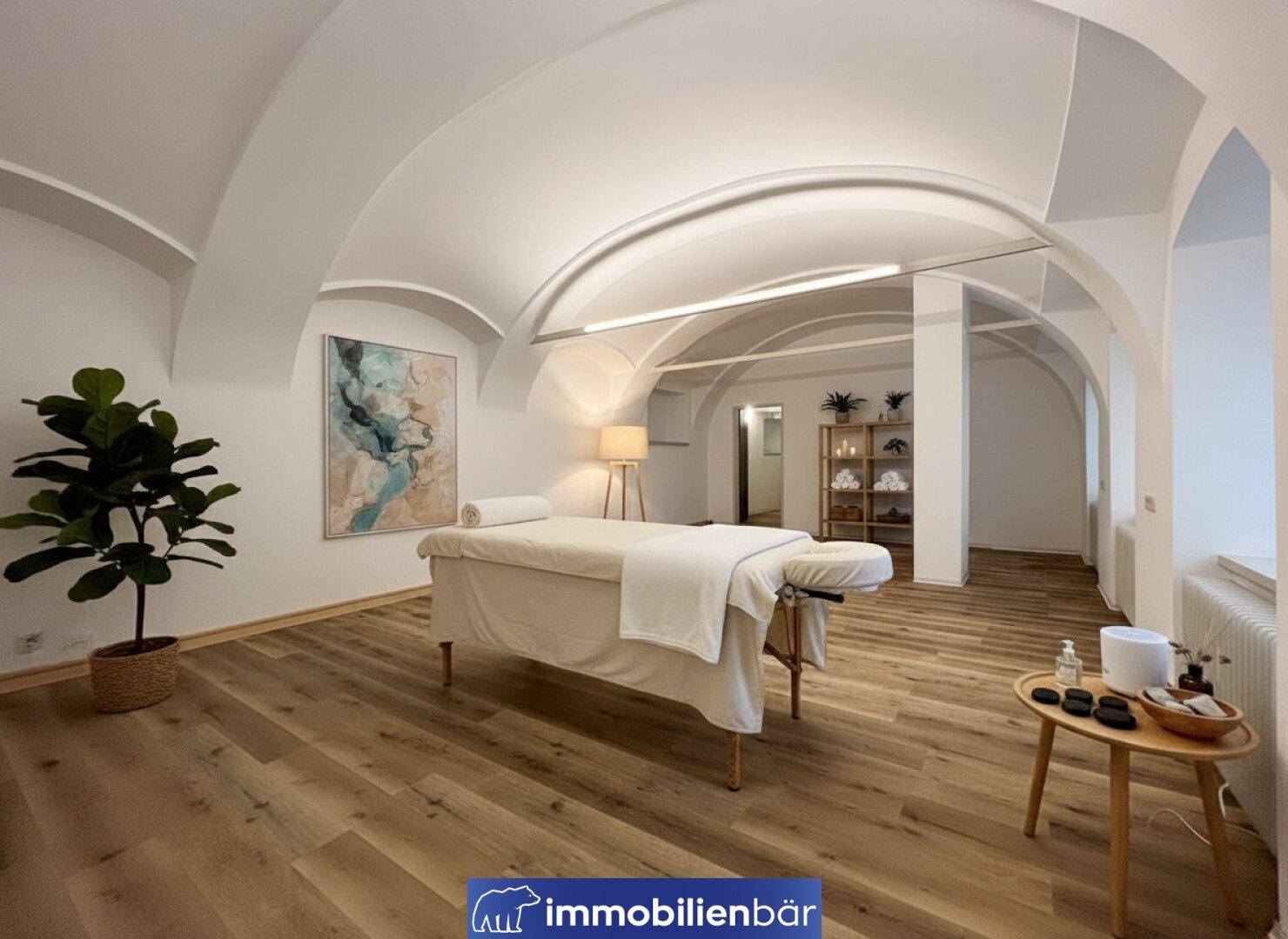 Ruhiger Behandlungsraum mit einer Massageliege, Holzboden und Kunstwerk an der Wand unter gewölbter Decke.