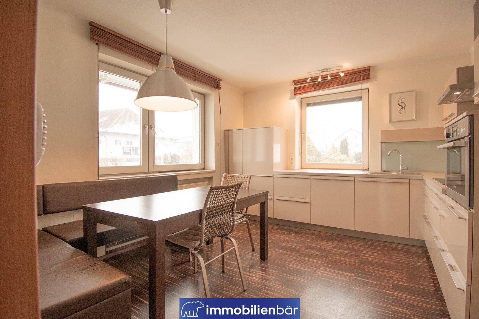 Moderne Einbauküche mit hellen Fronten, Essbereich und dunklem Holzfußboden.