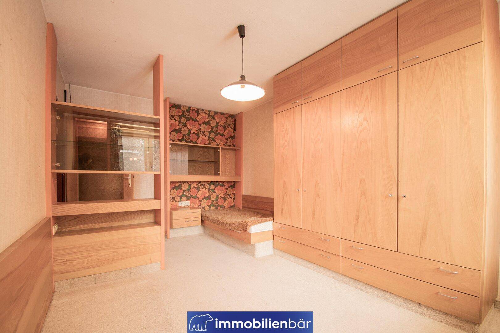 Schlafzimmer mit Einbauschränken aus hellem Holz und floraler Tapete an der Wand.