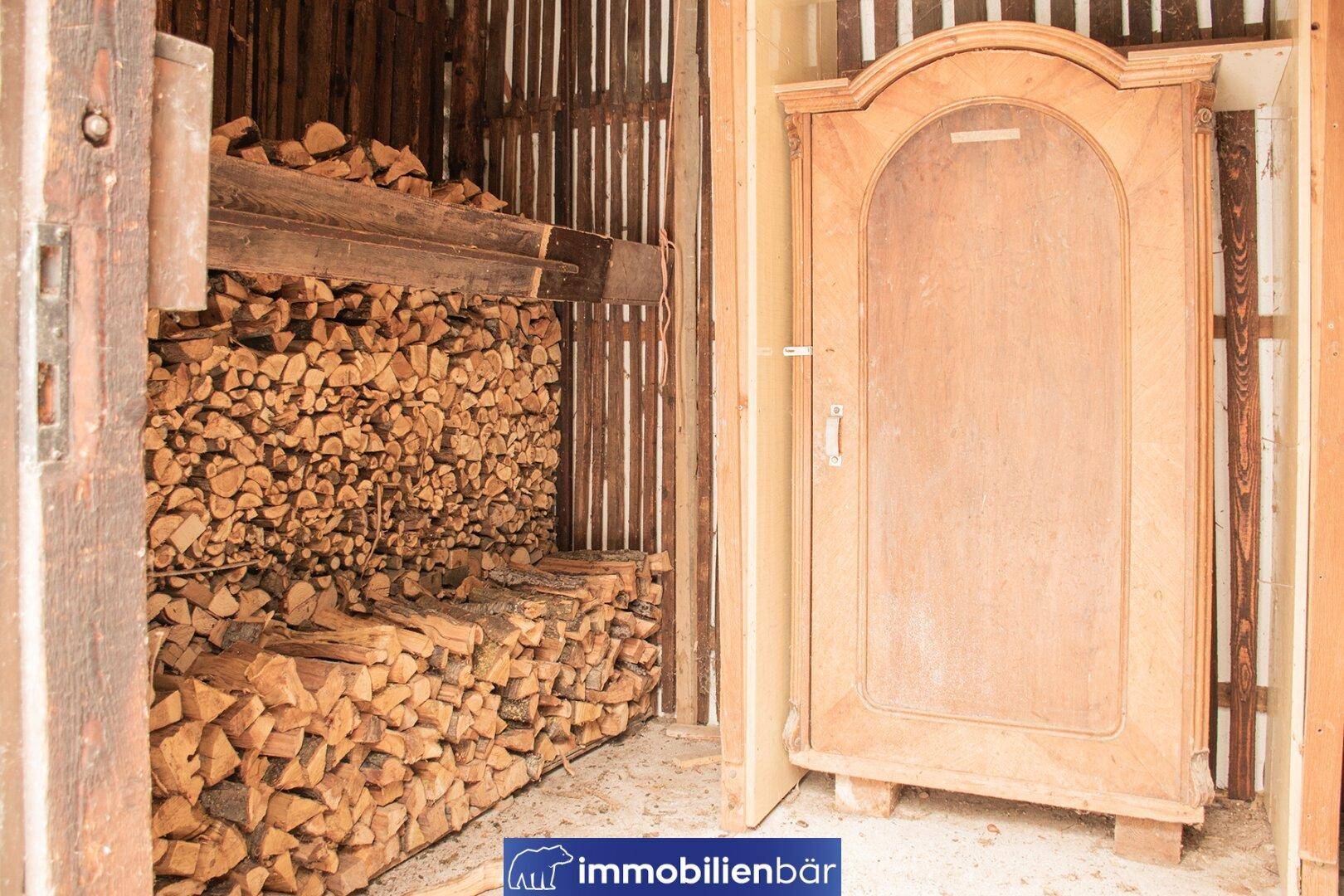 Rustikaler Lagerraum mit gestapeltem Brennholz und einem alten Holzschrank.