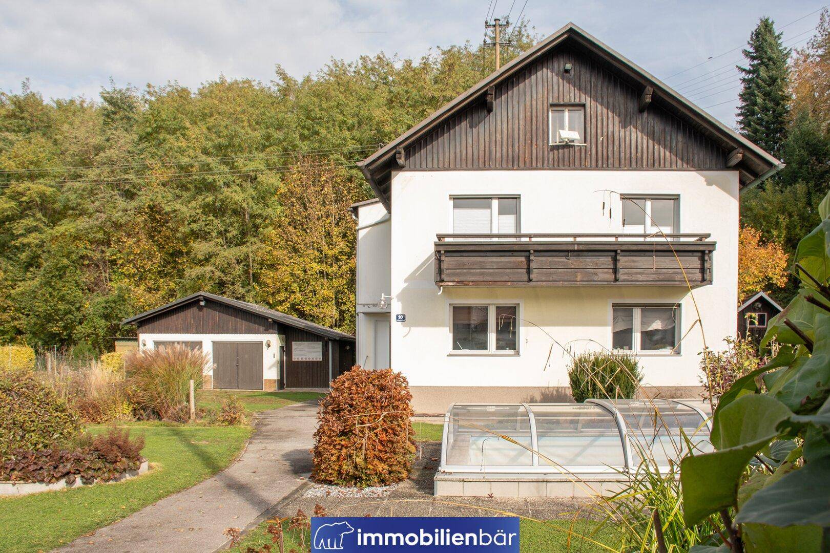Weißes Einfamilienhaus mit Satteldach, Garten und überdachtem Poolbereich im Grünen.