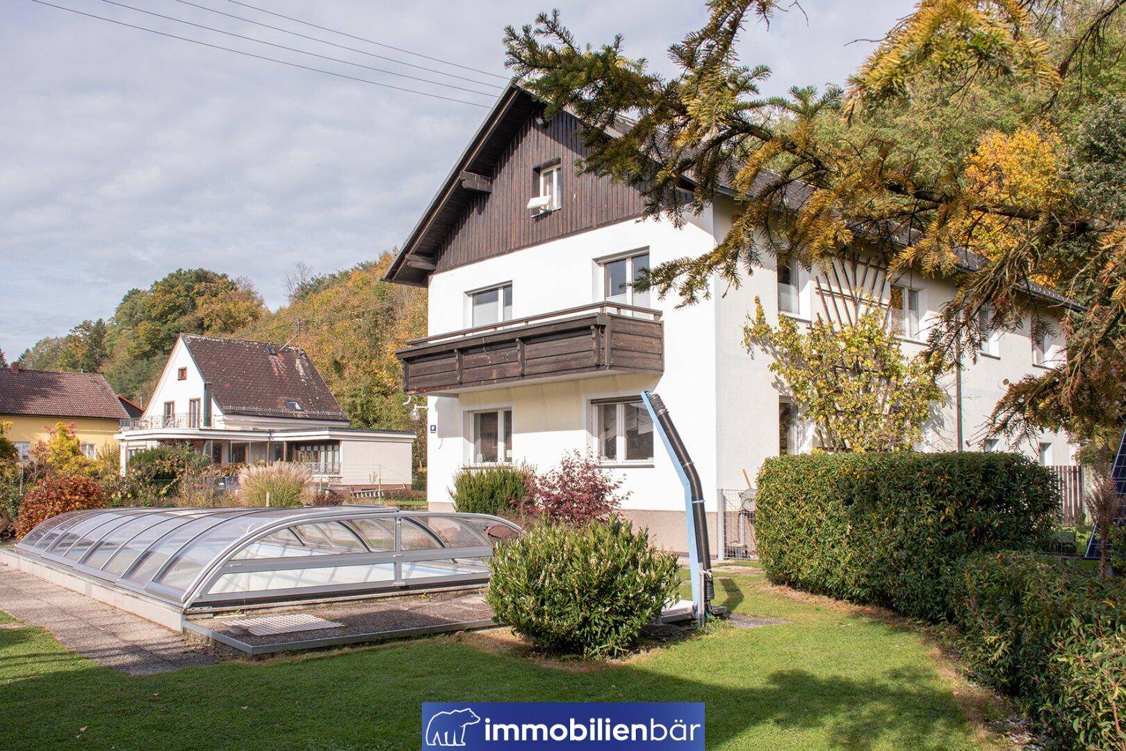 Seitenansicht des Hauses mit Garten, Hecke und einem überdachten Schwimmbecken.