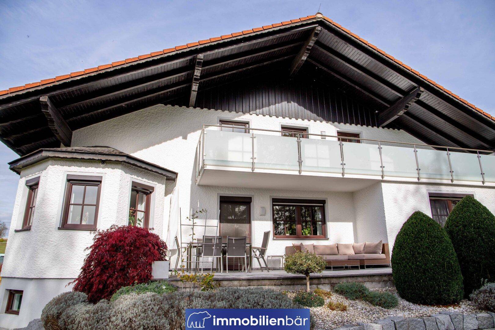 Nahaufnahme der Hausfassade mit möblierter Terrasse und modernem Balkon mit Glasgeländer.