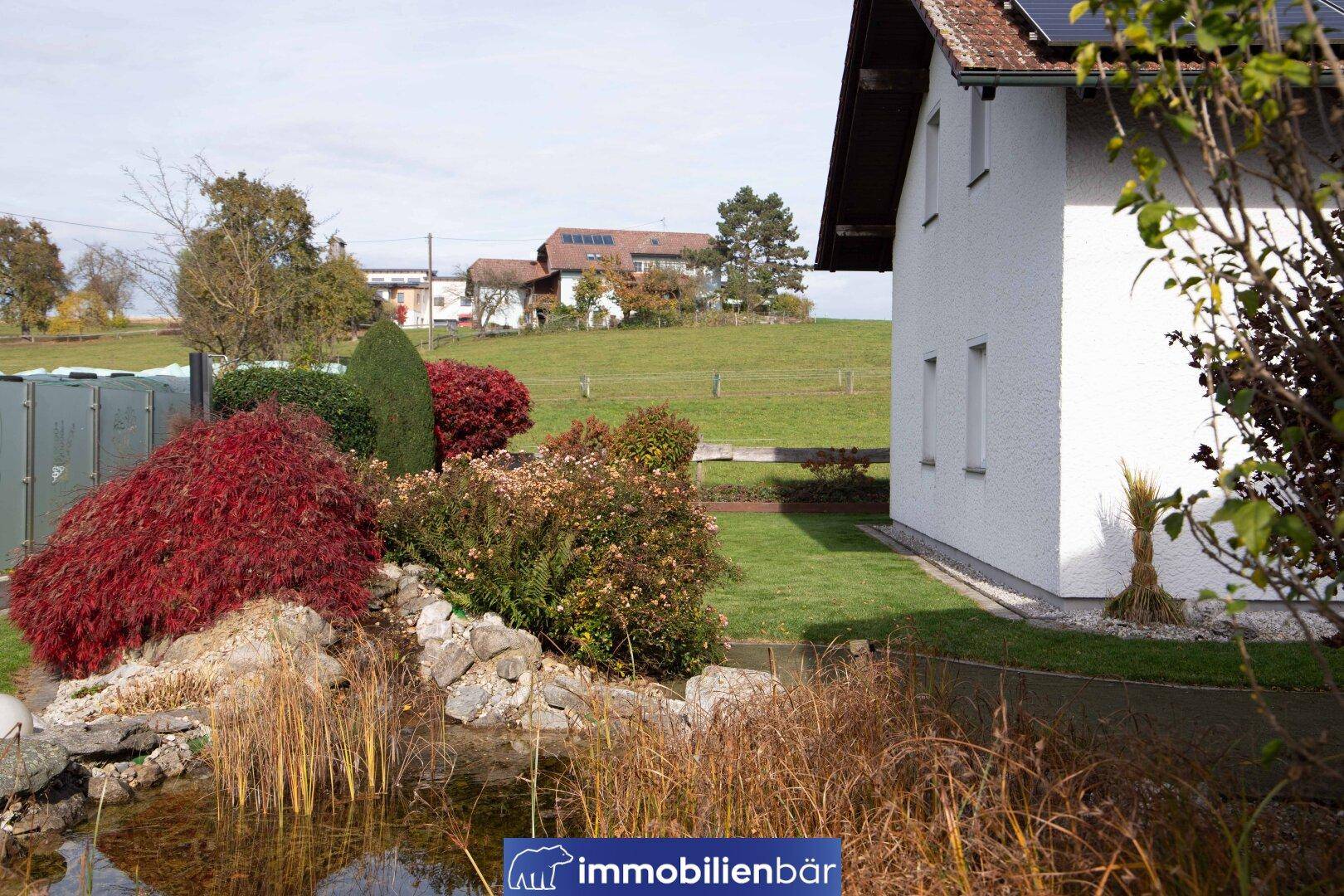 Gepflegter Gartenbereich mit Teich und herbstlicher Bepflanzung, umgeben von Grünflächen.