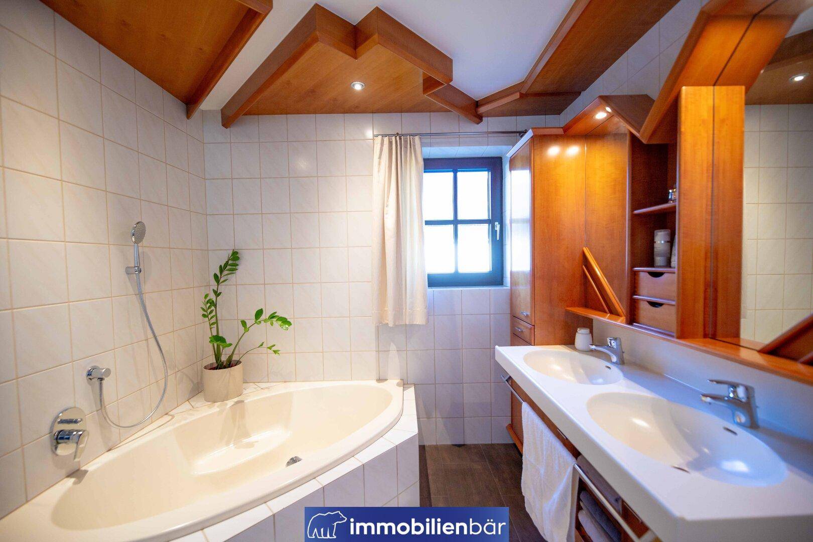 Geräumiges Badezimmer mit Doppelwaschbecken, Badewanne und Holzdecke, hell gefliest.
