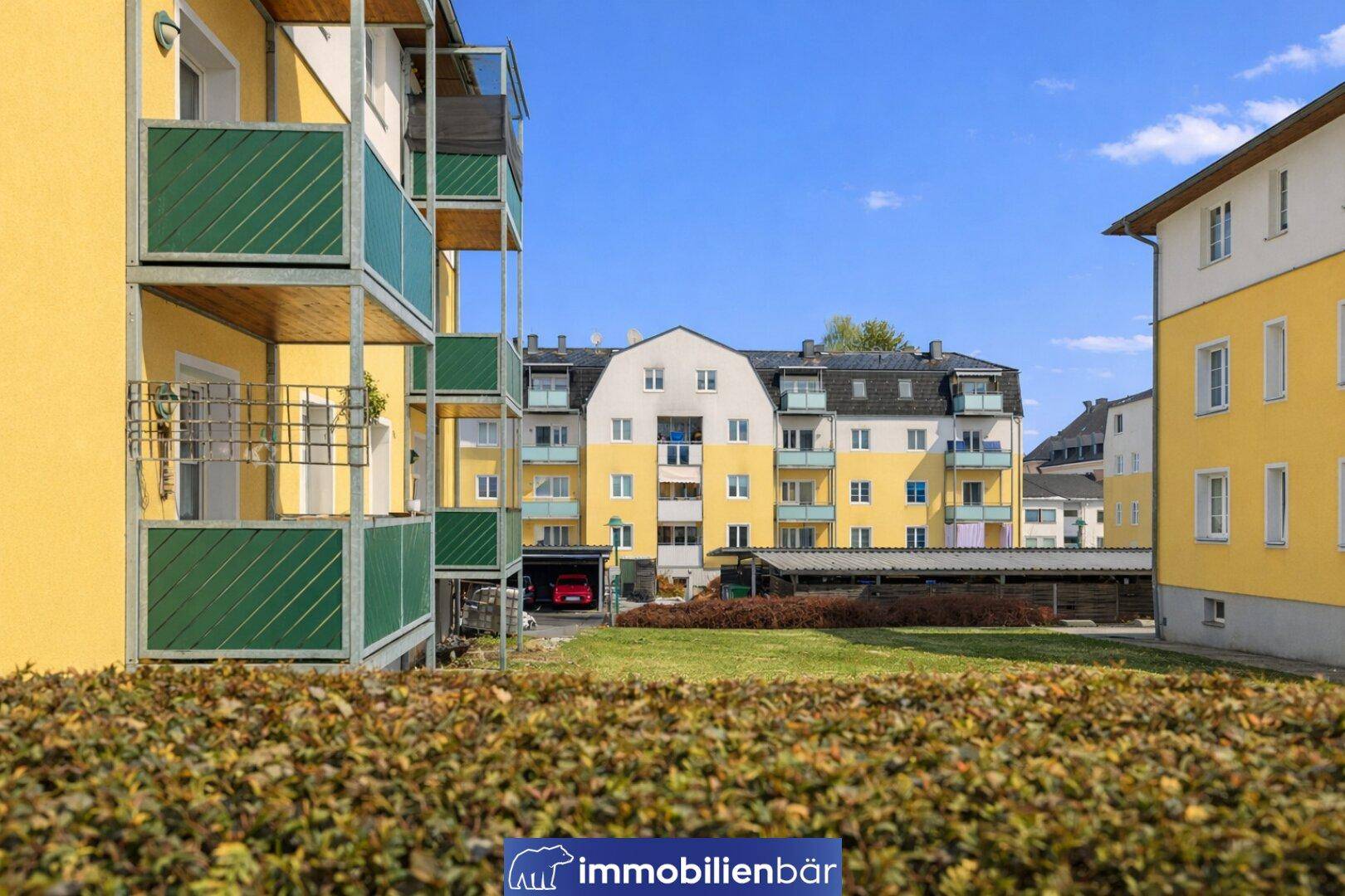 Wohnanlage mit gelben Fassaden, grünen Rasenflächen und Carports im Hintergrund.