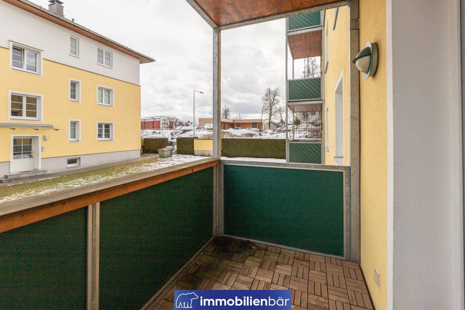 Überdachter Balkon mit Holzboden und Blick auf die umliegenden Gebäude und Winterlandschaft.