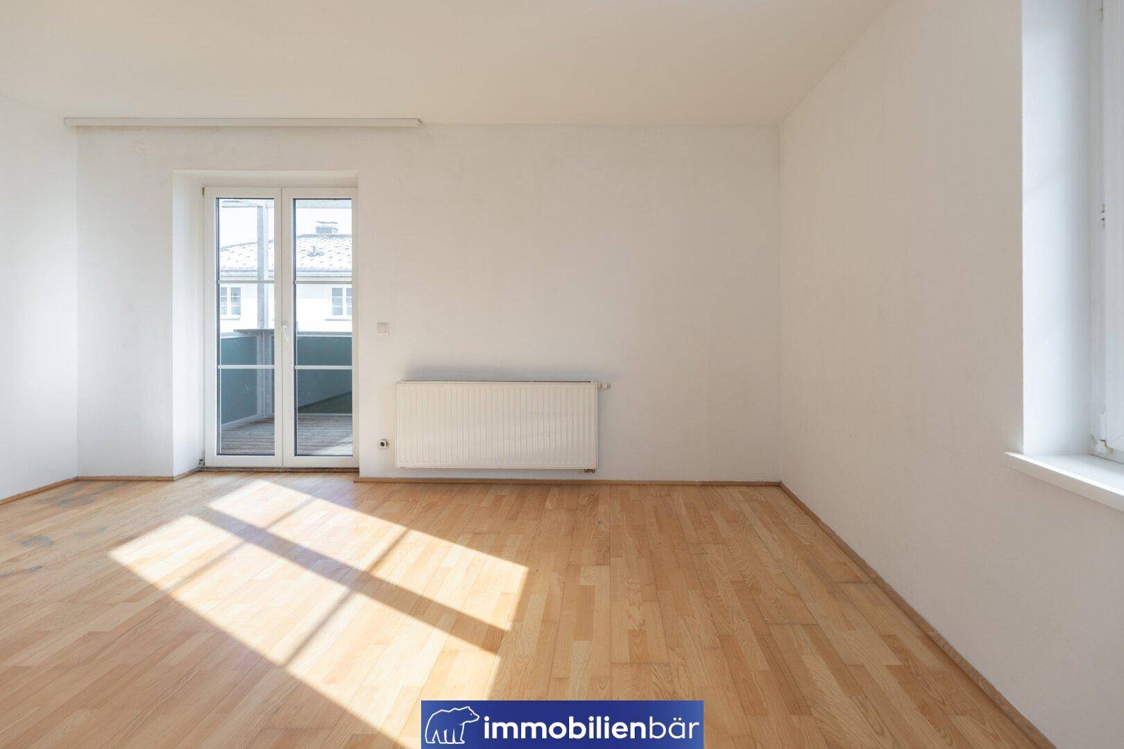 Helles Wohnzimmer mit Holzboden und Zugang zu einem Balkon, ideal für natürliche Belichtung.
