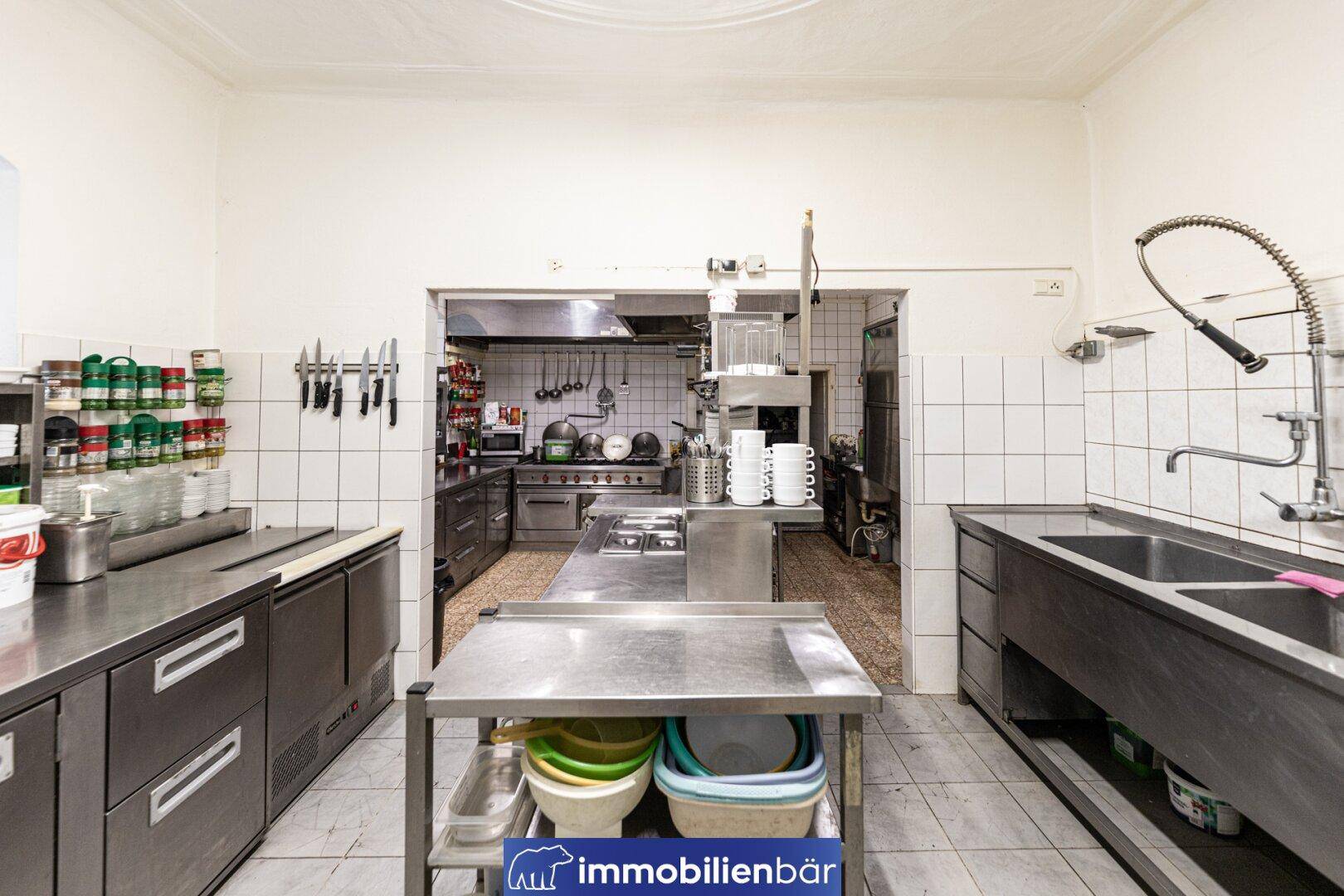 Professionelle Großküche mit Edelstahlgeräten, Fliesenwänden und Arbeitsflächen.