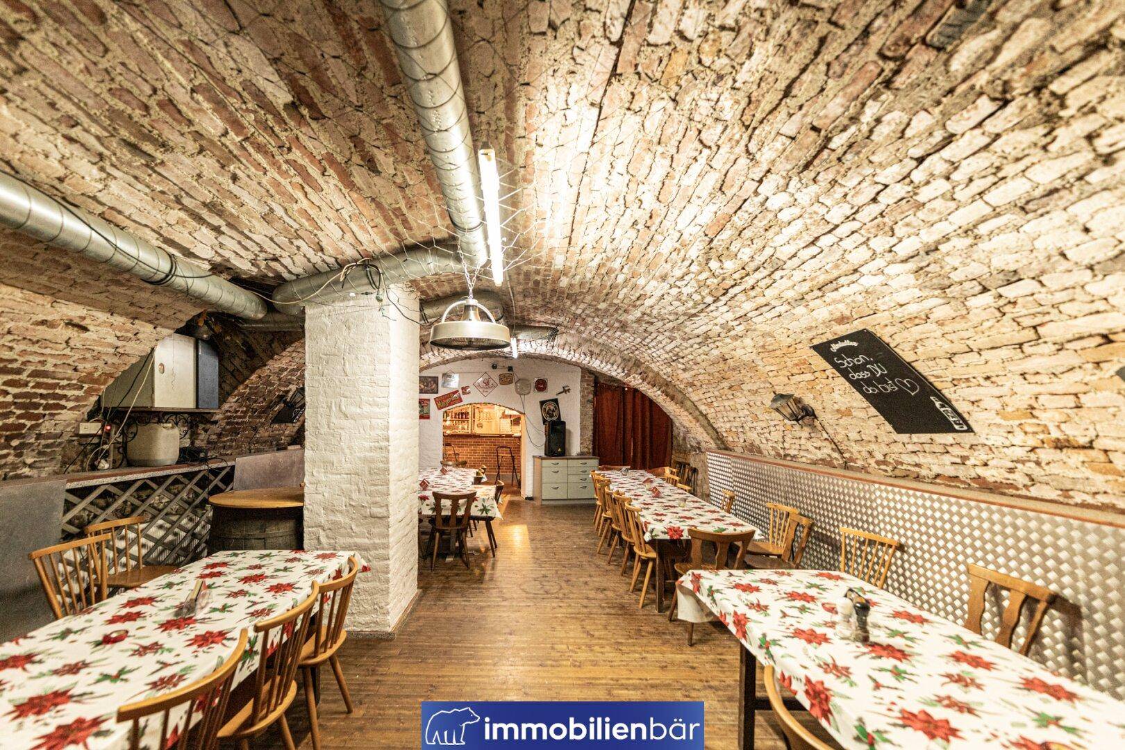Geräumiger Keller mit Ziegelgewölbe, Holzboden und rustikaler Einrichtung, ideal für Feiern.