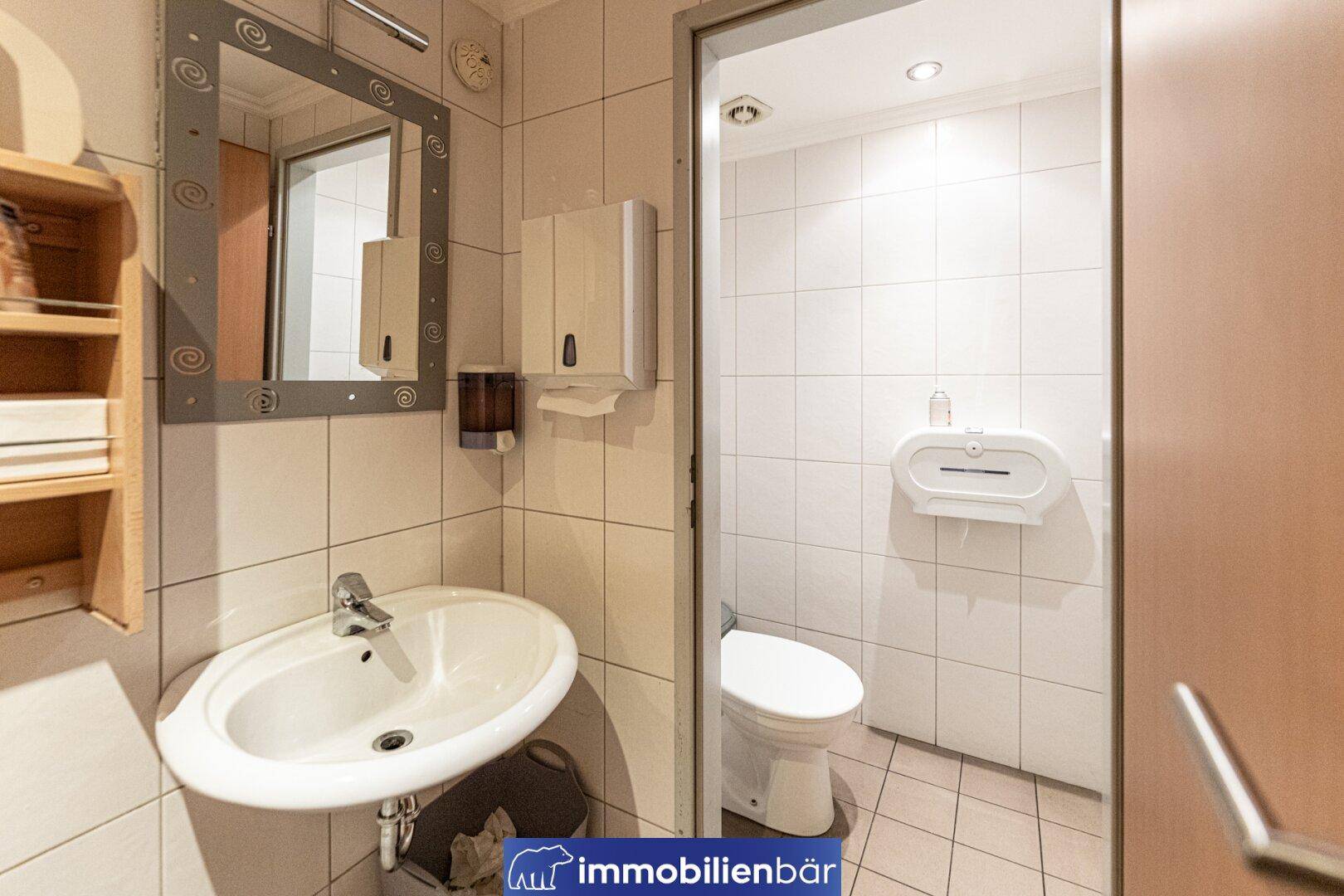 Helle Gästetoilette mit Waschbecken, Spiegel und weiß gefliesten Wänden.