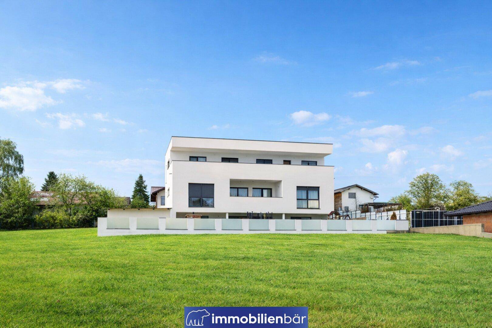 Zeitgenössisches Wohnhaus mit großen Fenstern und Balkon, umgeben von weitläufigen Grünflächen.