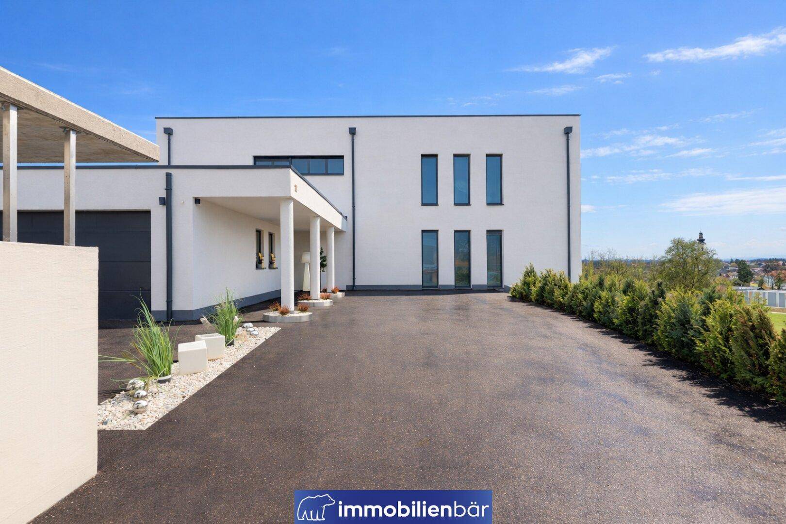 Moderne Hausfassade mit Einfahrt und Garage, umgeben von gepflegten Hecken und Kiesbeeten.