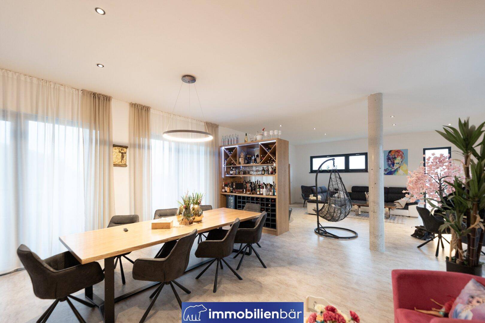 Offener Wohn- und Essbereich mit großem Holztisch, Weinschrank und gemütlicher Sitzecke.