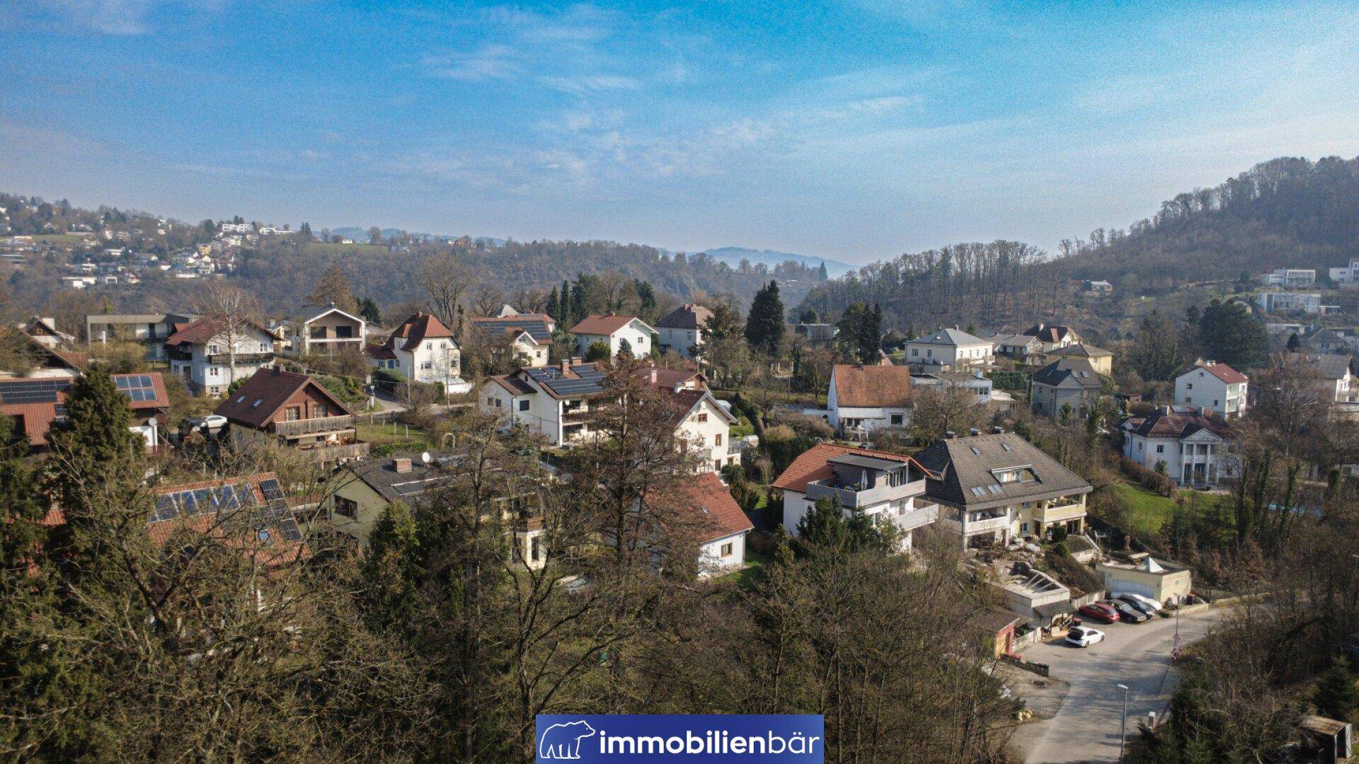 Panoramablick auf eine Wohnsiedlung mit vielen Häusern und grünen Hügeln im Hintergrund.