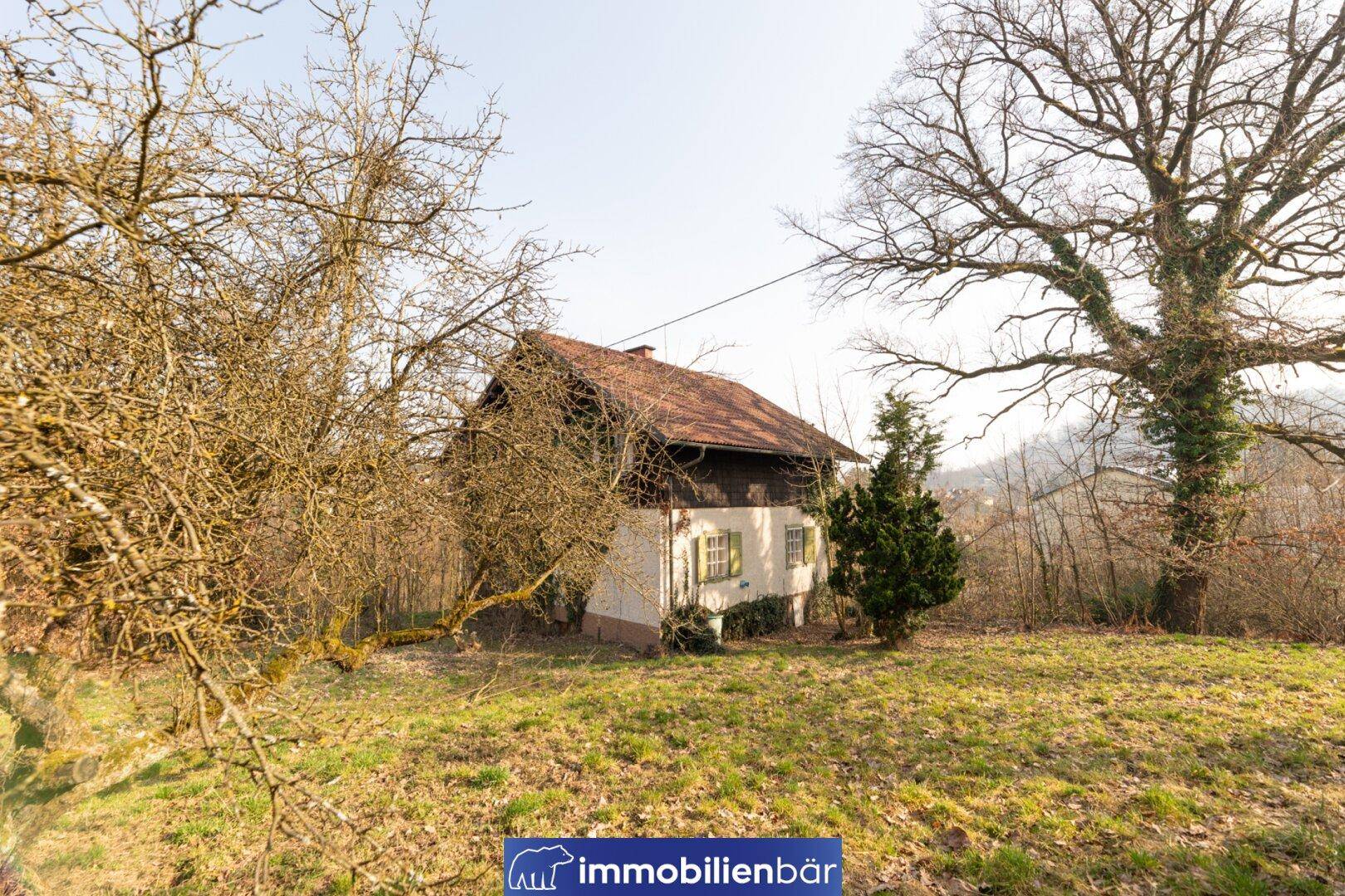 Altes Haus mit rotem Ziegeldach, umgeben von kahlen Bäumen und einem großen Garten.