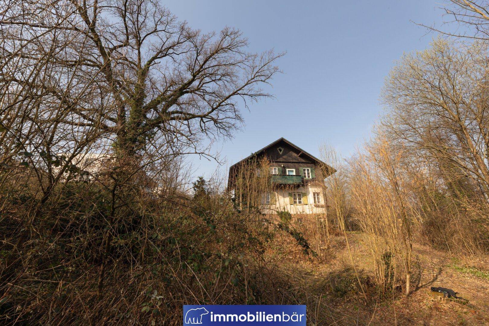 Traditionelles Haus auf einem Hügel, umgeben von kahlen Bäumen und Sträuchern.