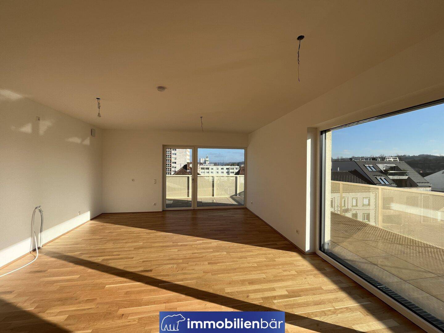 Lichtdurchfluteter Wohnraum mit Eichenparkett und Zugang zu einem großen Balkon.
