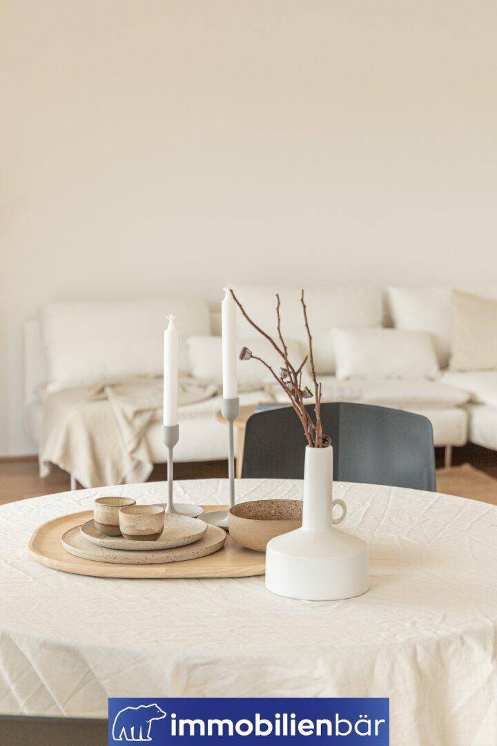 Heller Wohnbereich mit stilvoller Dekoration und gemütlichem Sofa im Hintergrund.
