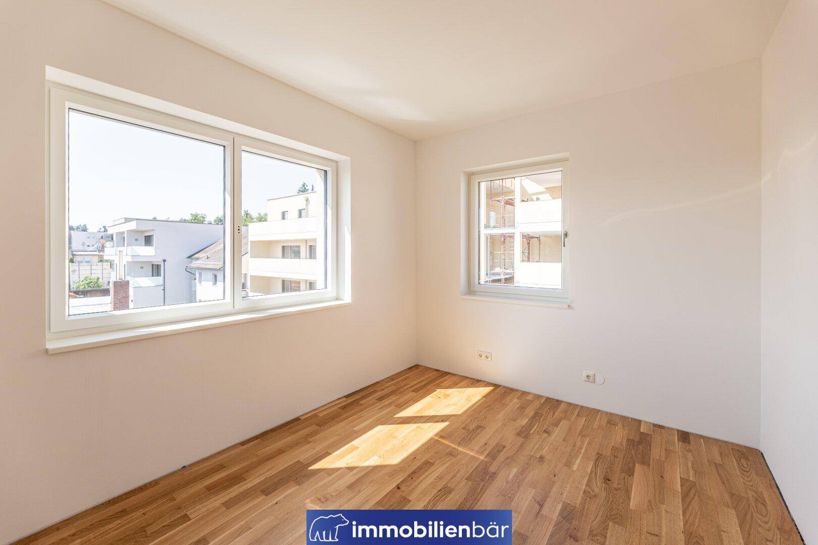 Helles Schlafzimmer mit Parkettboden und großen Fenstern für viel Tageslicht.