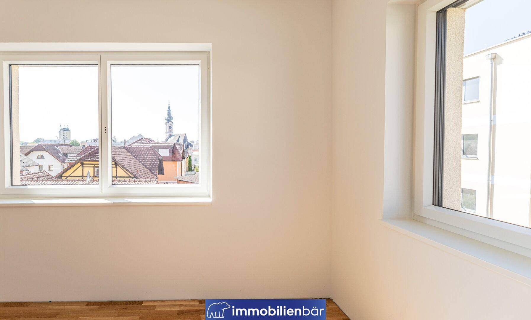 Sonnenlichtdurchflutetes Zimmer mit Parkettboden und Blick auf die Stadt.