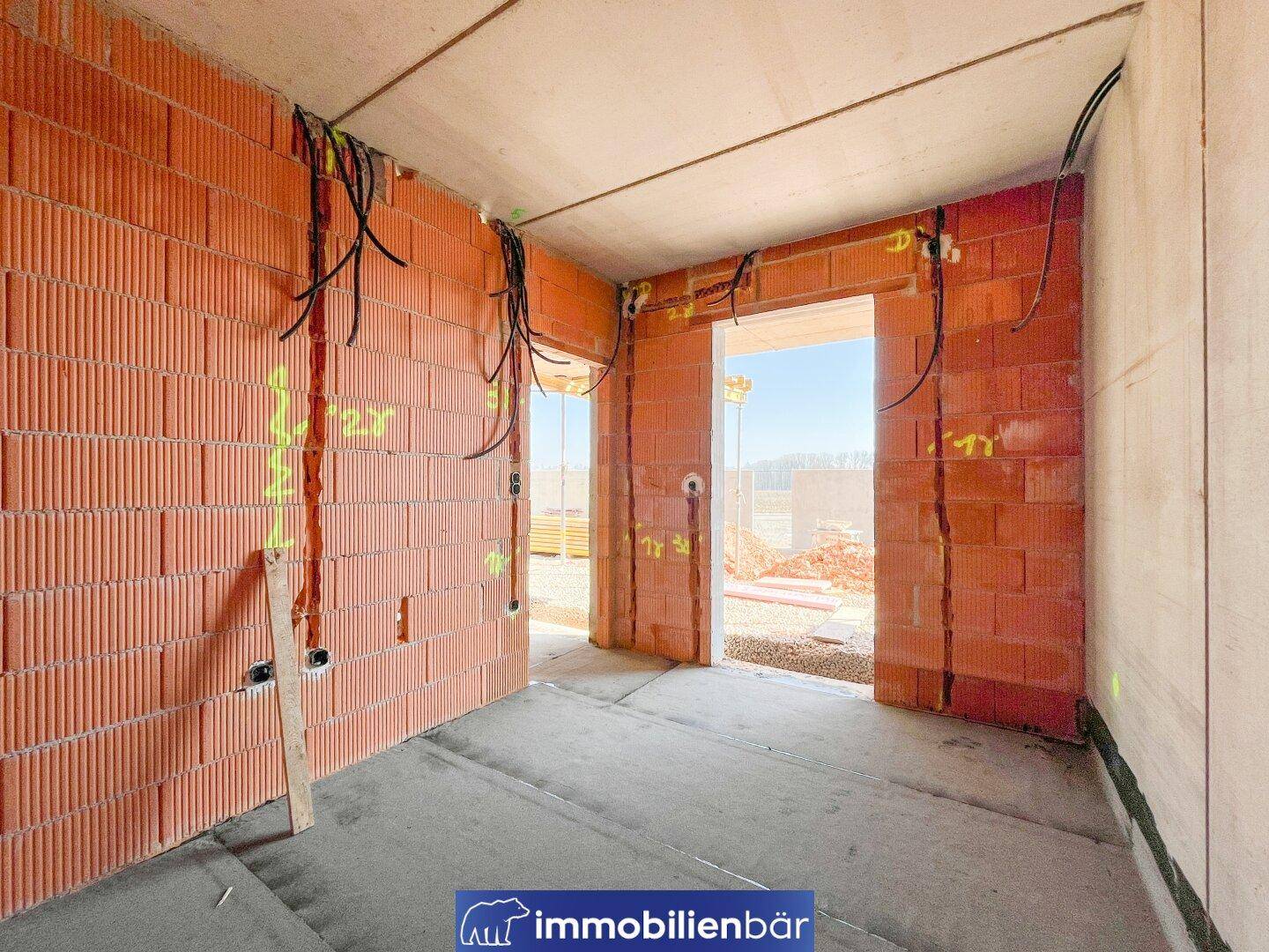 Rohbau-Innenansicht mit sichtbaren Ziegelwänden und vorbereiteten Elektroinstallationen.