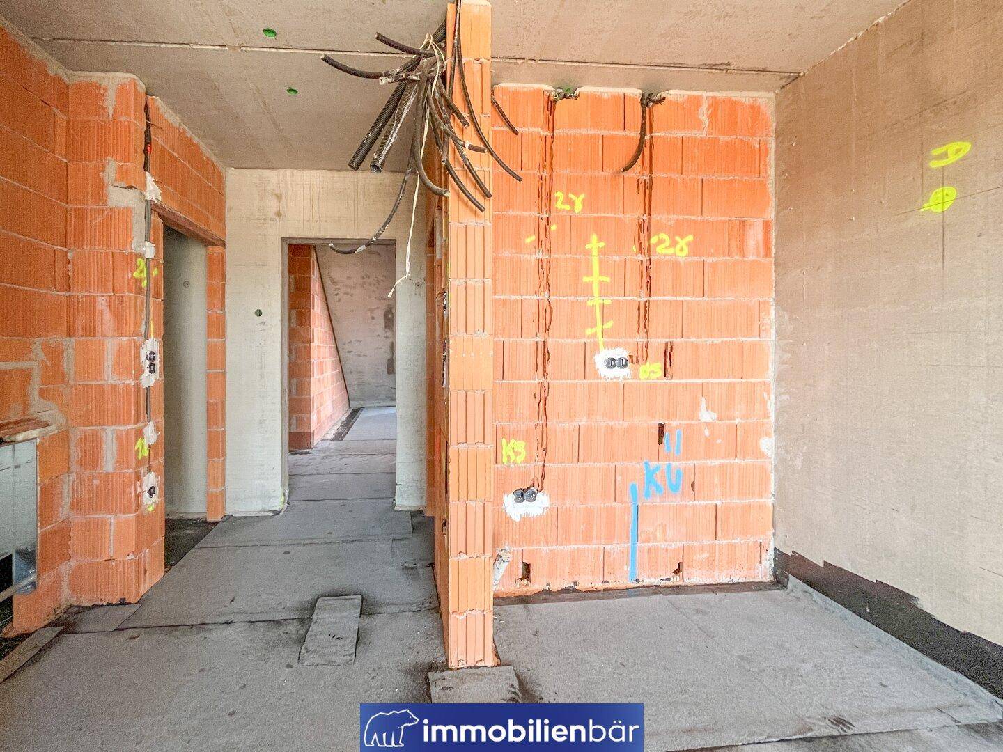 Rohbau-Innenraum mit Ziegelwänden, vorbereiteten Leitungen und Blick in weitere unfertige Räume.