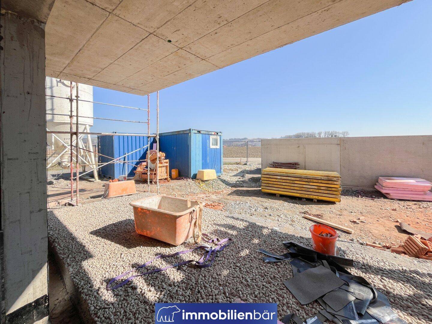 Baustelle des Neubaus mit Containern und Baumaterialien unter blauem Himmel.