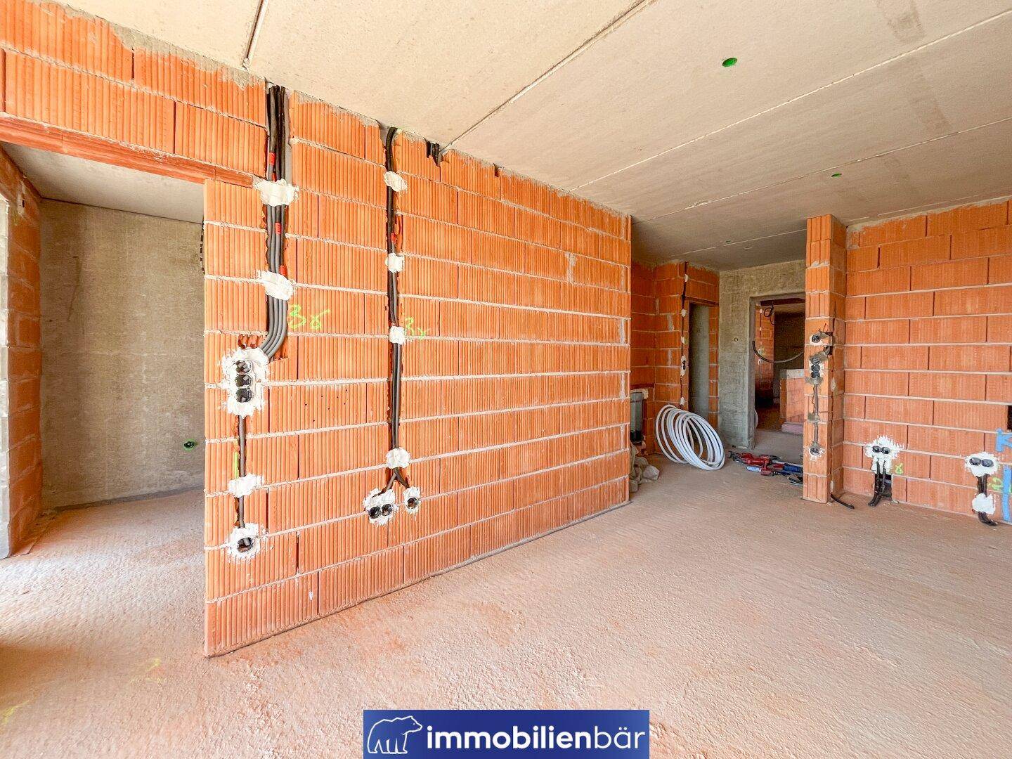Rohbau-Innenraum mit Ziegelwänden und sichtbaren Elektroinstallationen für zukünftige Steckdosen.