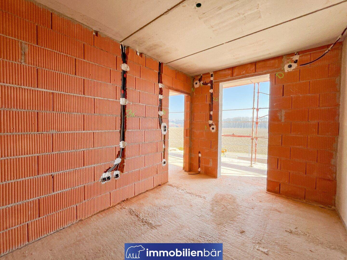 Heller Rohbau-Raum mit Ziegelwänden und weitem Blick auf die umliegende Landschaft.
