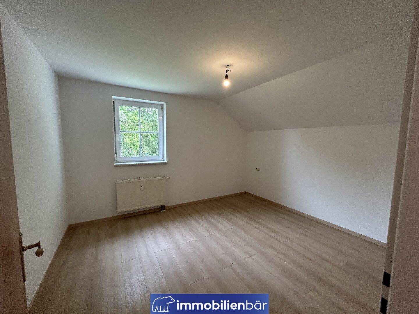 Ruhiges Zimmer im Dachgeschoss mit Laminatboden und einem Fenster mit Blick ins Grüne.