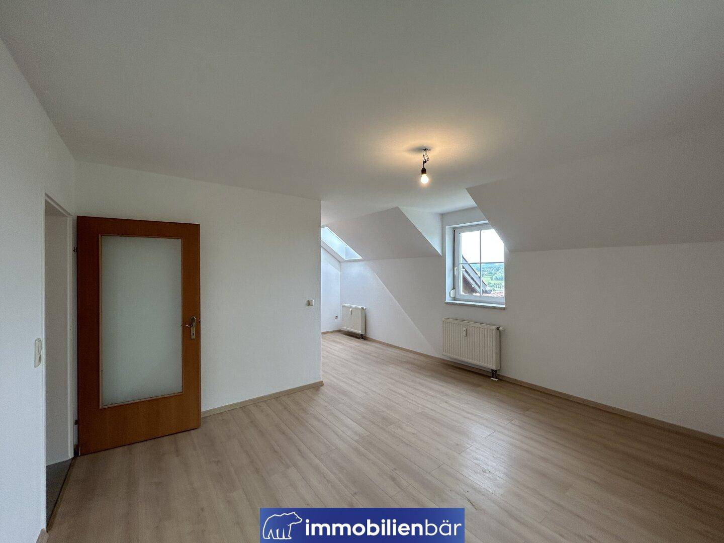 Helles Zimmer im Dachgeschoss mit Laminatboden, Dachschrägen und einem Fenster mit Ausblick.