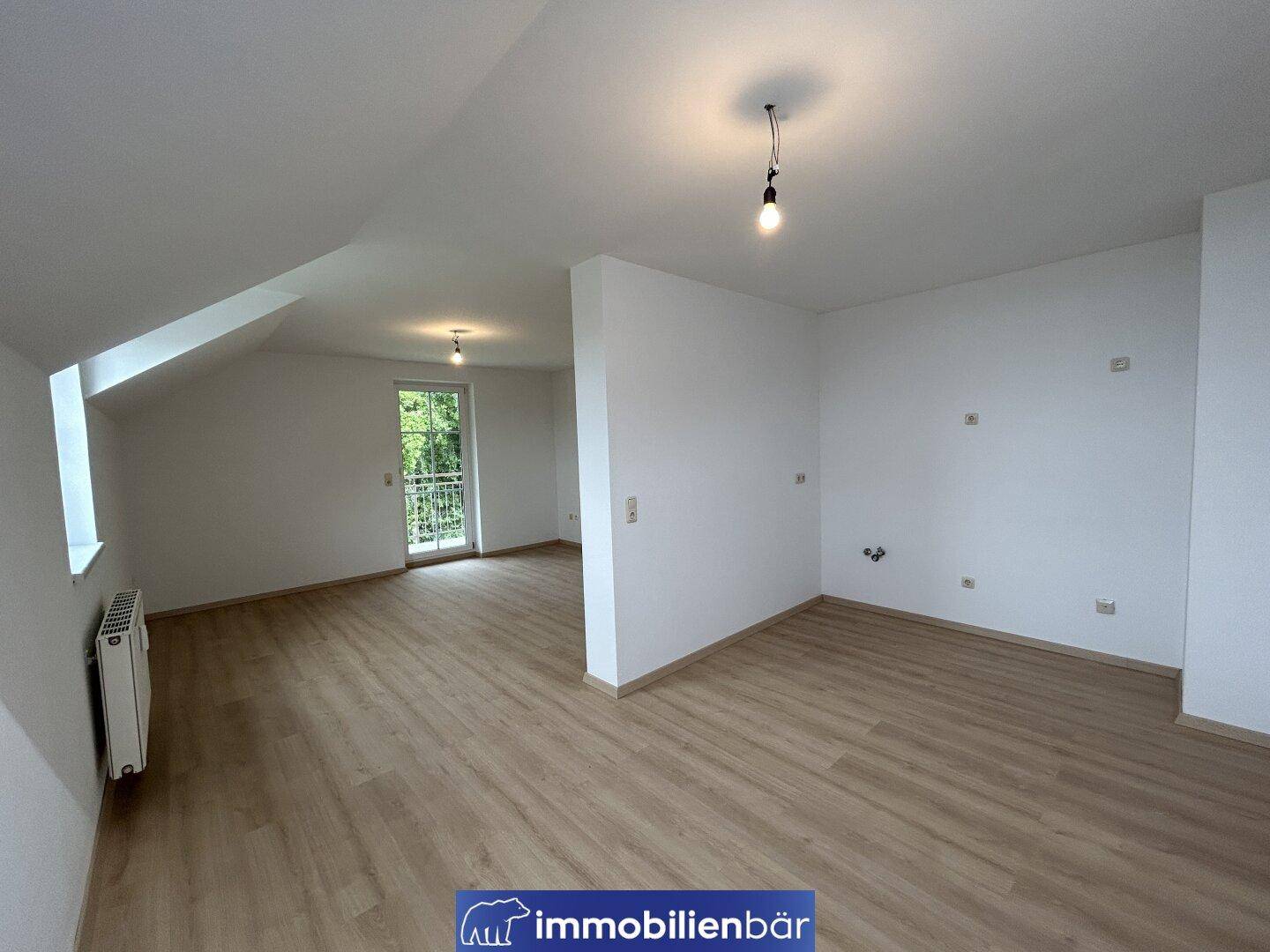 Offener Wohnbereich im Dachgeschoss mit Laminatboden, Dachschrägen und Balkonzugang.