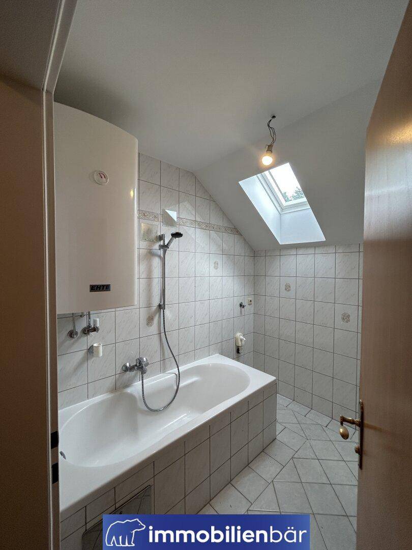 Gefliestes Badezimmer im Dachgeschoss mit Badewanne, Dusche und Dachfenster für Tageslicht.