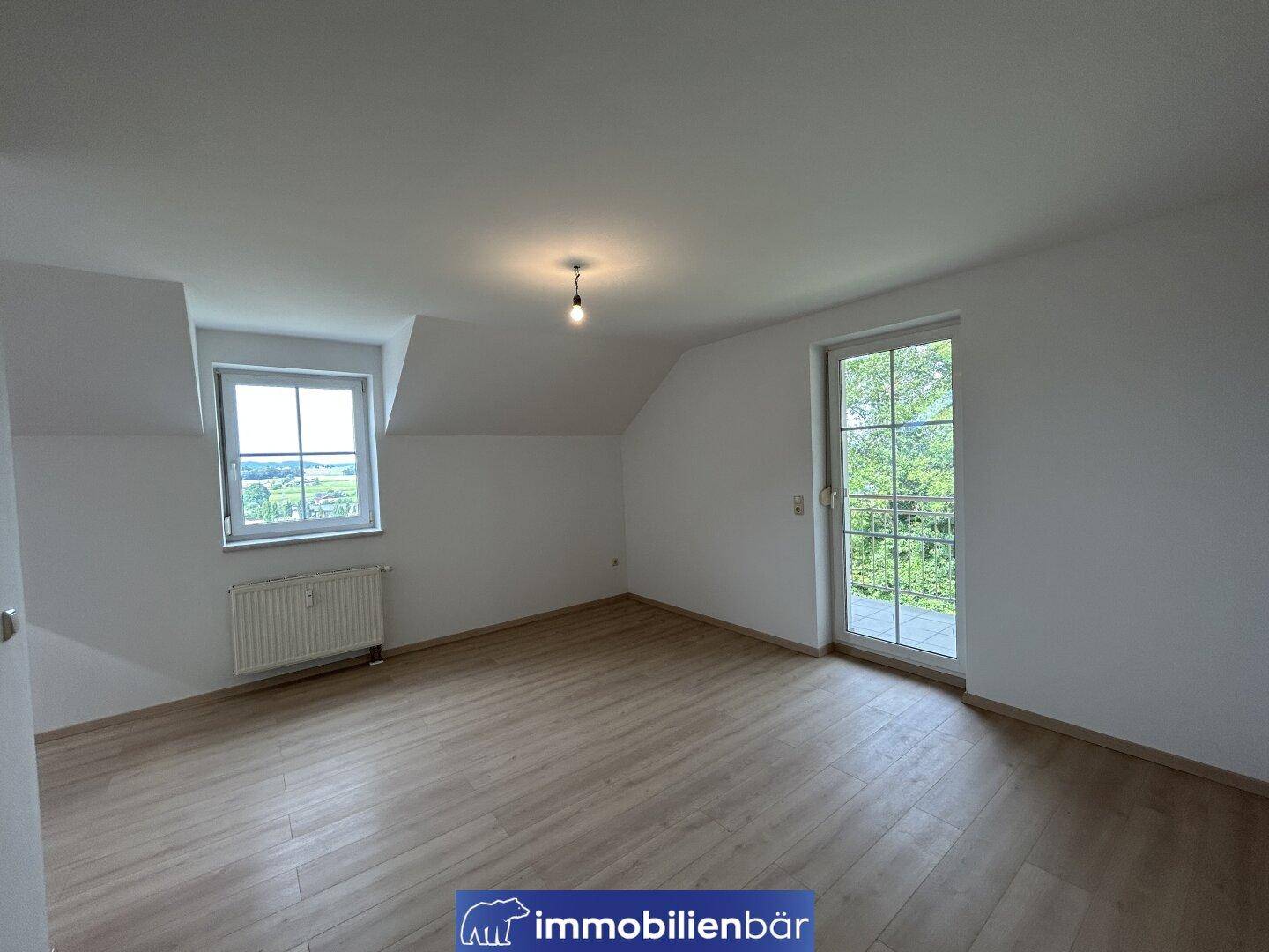 Geräumiges Zimmer im Dachgeschoss mit Laminatboden und Zugang zu einem Balkon.