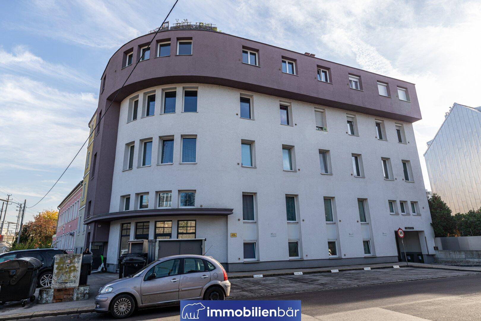 Gesamtansicht der modernen Gebäudefassade mit abgerundeten Ecken und vielen Fenstern an einem sonnigen Tag.